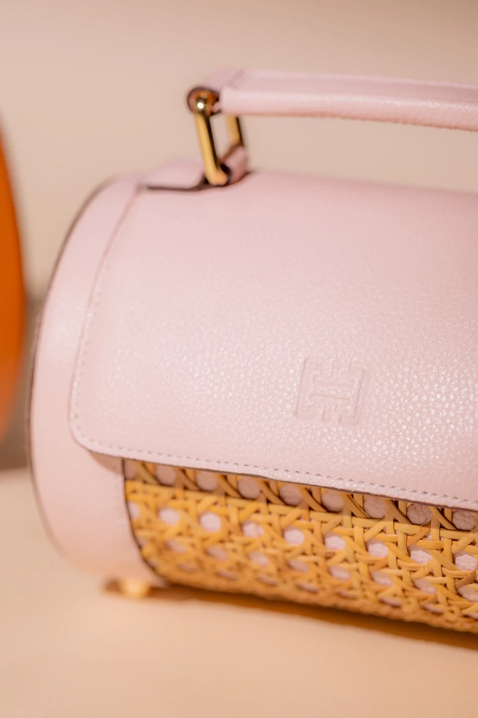 Close-up of the pale pink leather flap, gold handle fitting and solihiya weave of a Rollers Mini.